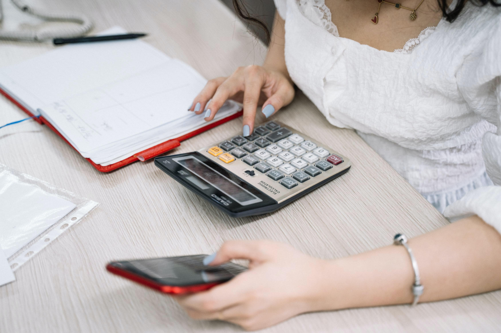 woman making notes and using a calculator whilst wearing a white top.