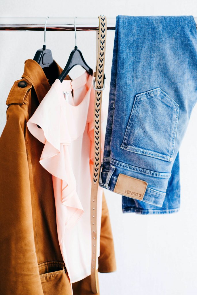 a clothing rail with a pale pink t-shirt, a belt and pair of jeans hanging over the rail.