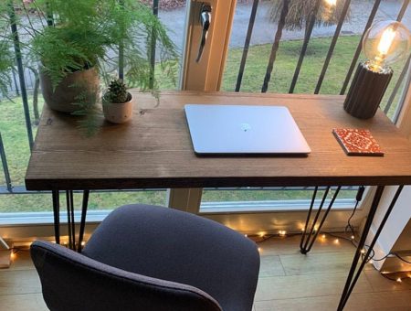desk with candle and laptop placed on top facing out of a window onto some greenery.