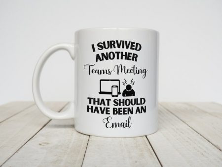 a white mug on a light wooden floor, the mug reads 'i survived another teams meeting that should have been an email'.