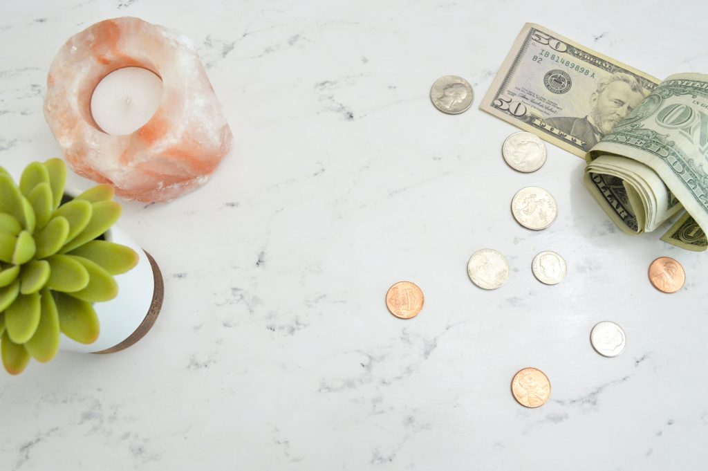a marble worktop pictured with a candle, a small succulent plant and a spread out variety of coins and notes.