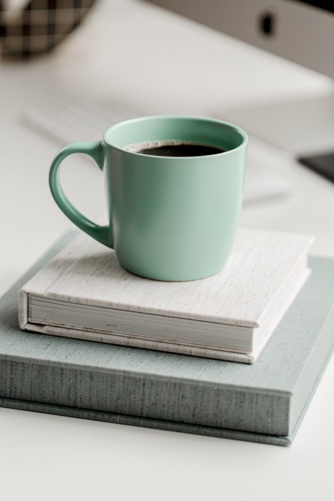a mint green mug full of a black coffee sat on top of two pale books.