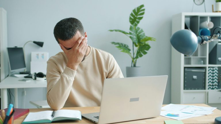 a man sitting at a desk in front of a computer with his head in his hand - frustrated