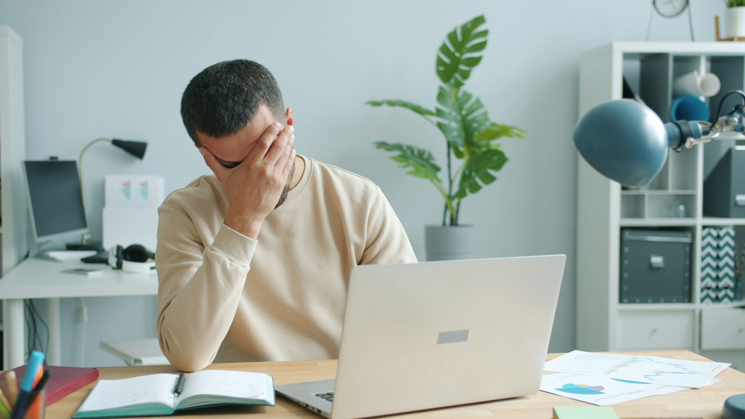 a man sitting at a desk in front of a computer with his head in his hand - frustrated