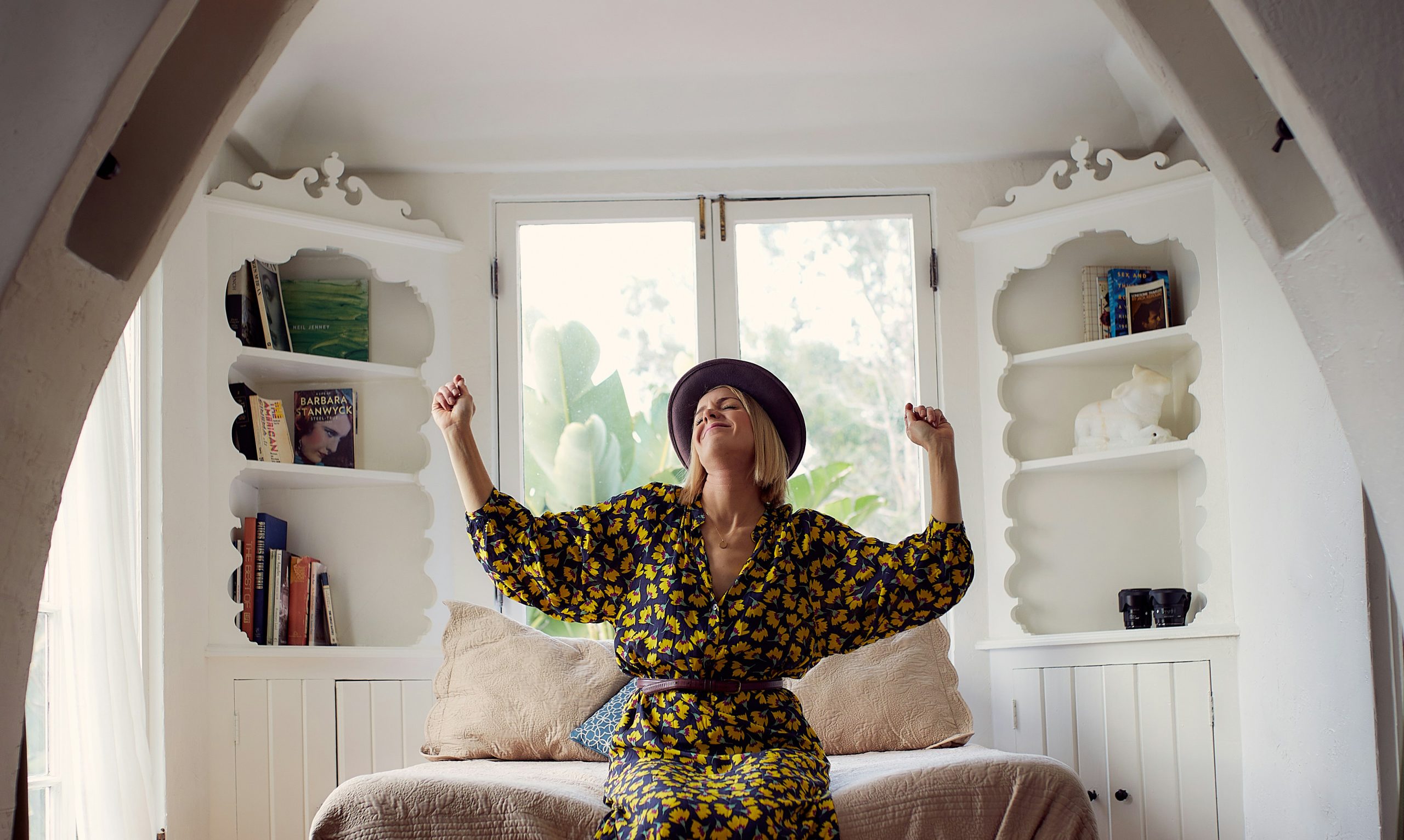 woman wearing a lemon-patterned dress is sat upon a chair with both hands raised in celebration.