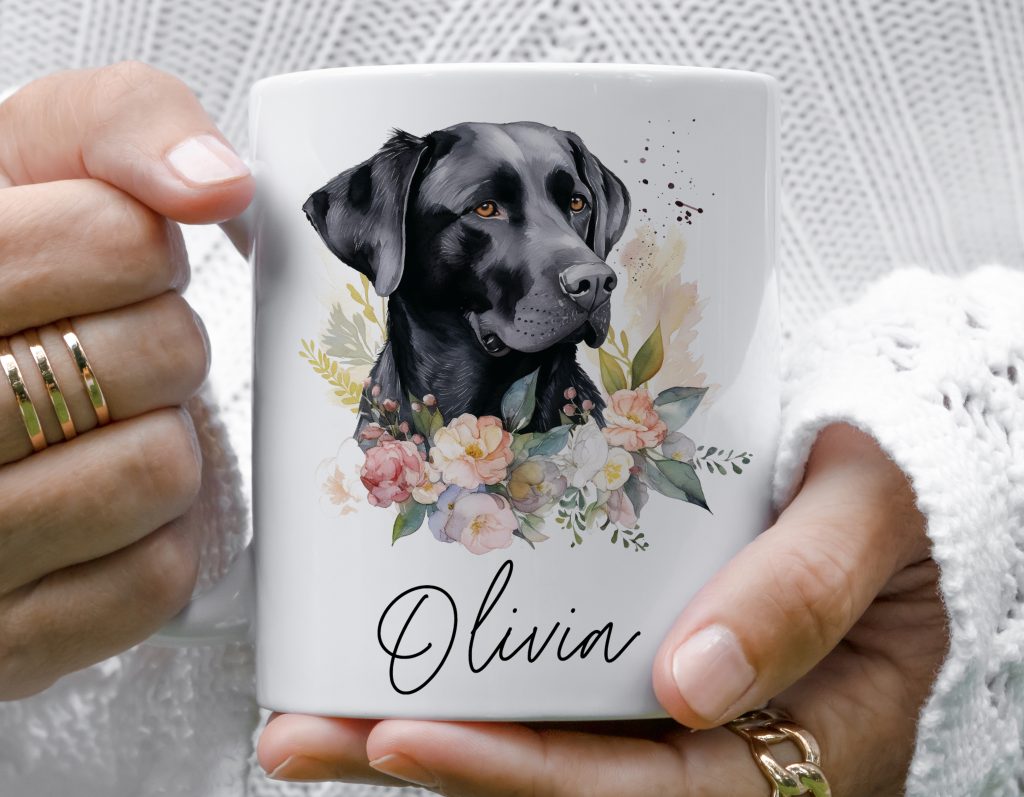 a white mug feautring a watercolour design of a black labrador alongside a select few flowers, in pink/beige tones, followed by a personalised name.