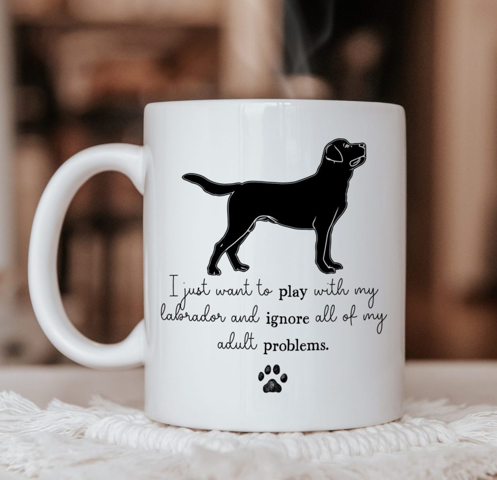 a white ceramic mug pictured on a material coaster, with the mug design showing a labrador silhouette with the phrase 'i just want to play with my labrador and ignore all of my adult problems'.